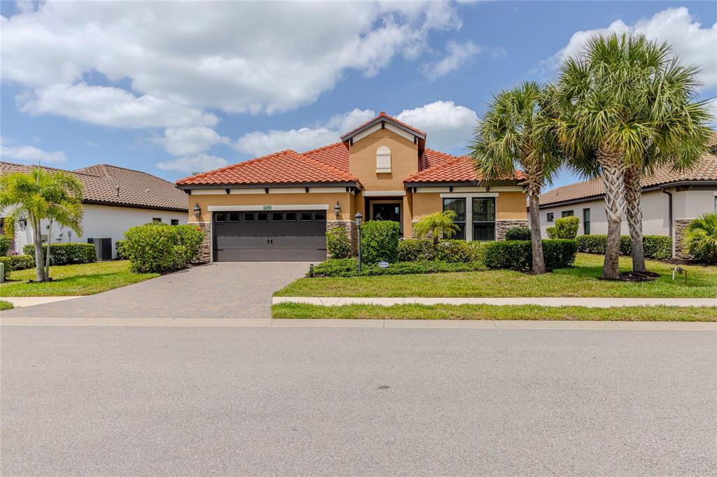 A single-story house with a terracotta tile roof, tan stucco walls, and a paved driveway — 26858 WEISKOPF DRIVE, ENGLEWOOD, FL