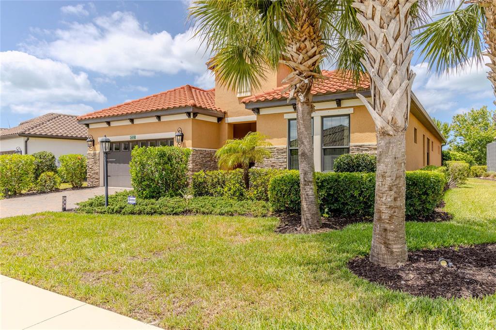 A single-story house with a tile roof, stucco exterior, and stone accents sits behind landscaping — 26858 WEISKOPF DRIVE, ENGLEWOOD, FL