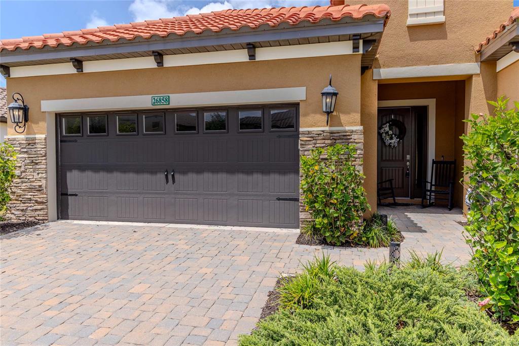 A tan house exterior features a gray garage door, stone accents, and a tiled roof — 26858 WEISKOPF DRIVE, ENGLEWOOD, FL