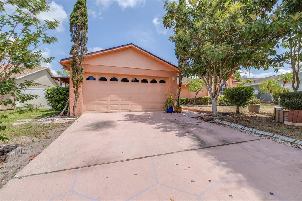 A peach-colored house with a two-car garage and a paved driveway under a blue sky — 2538 COUNTRYSIDE PINES DRIVE, CLEARWATER, FL