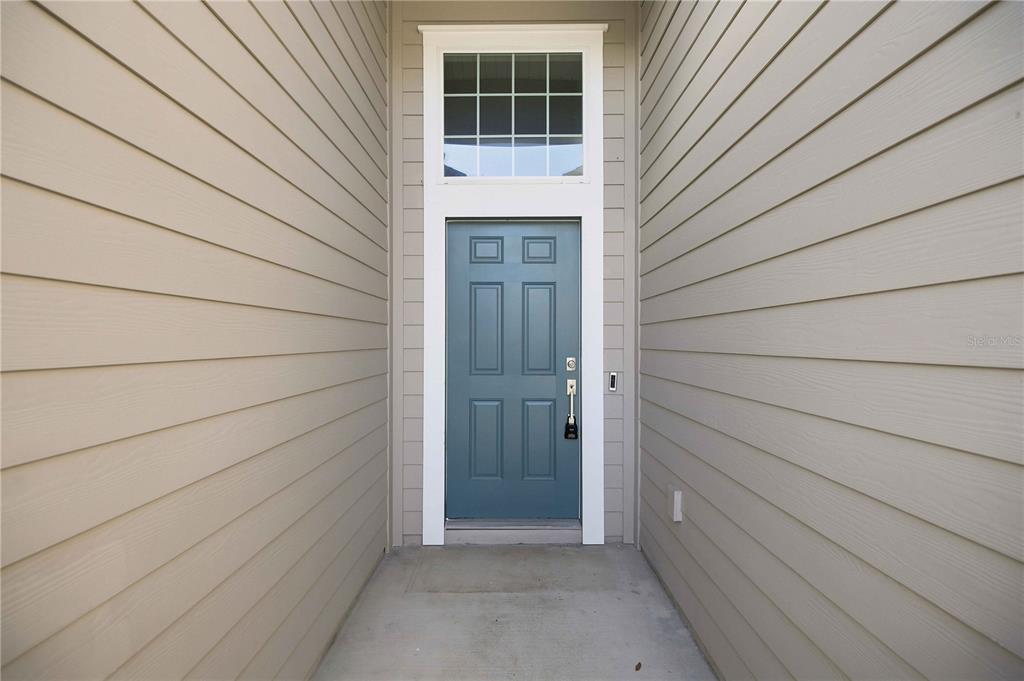 A blue front door with a transom window is set between beige horizontal siding walls — 3492 NE 38TH LANE, OCALA, FL