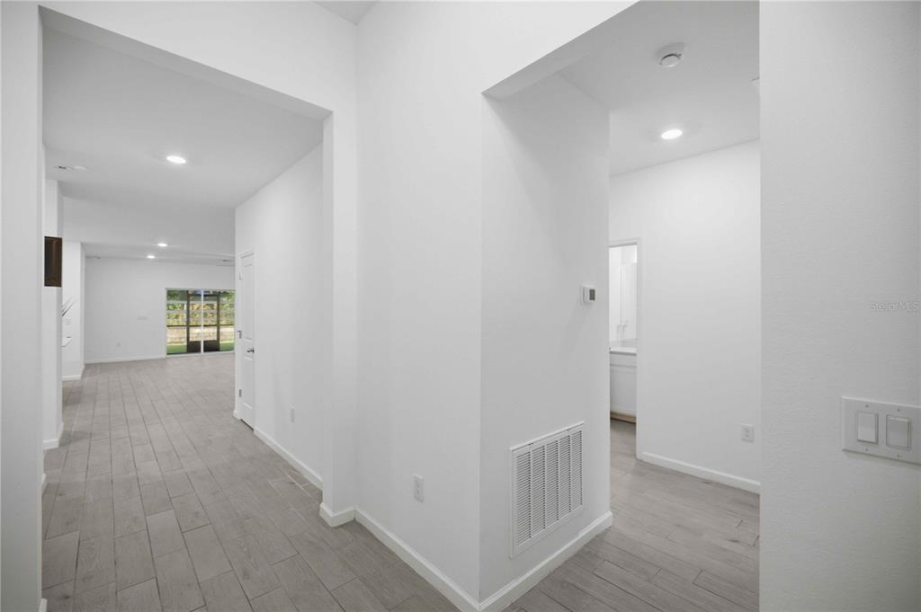A bright hallway with light wood-look tile flooring leads toward a living area with windows — 3492 NE 38TH LANE, OCALA, FL