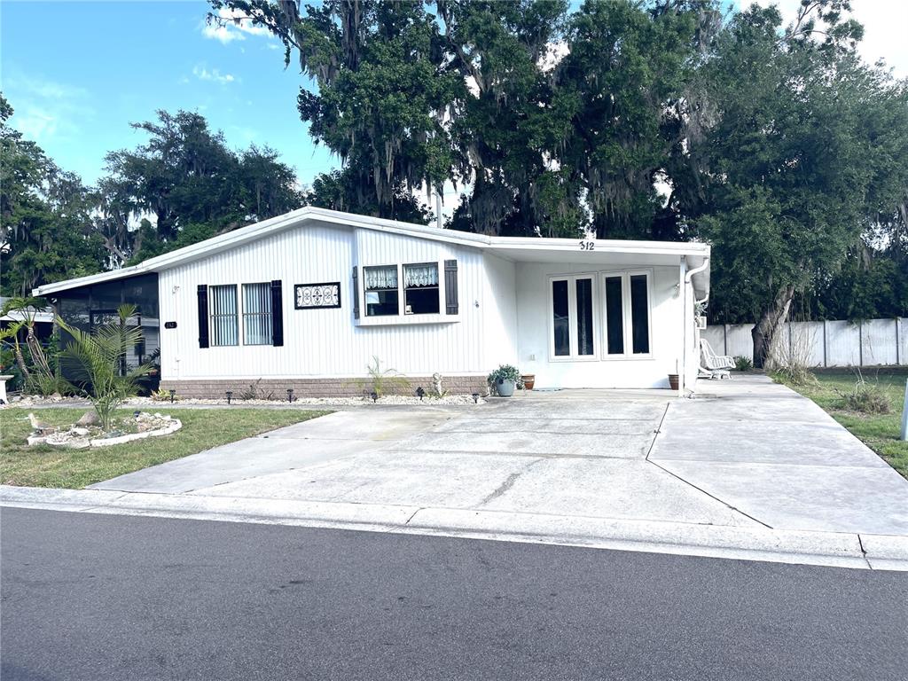 A white single-story manufactured home with a concrete driveway and a screened-in porch — 312 S TIMBER TRL, WILDWOOD, FL
