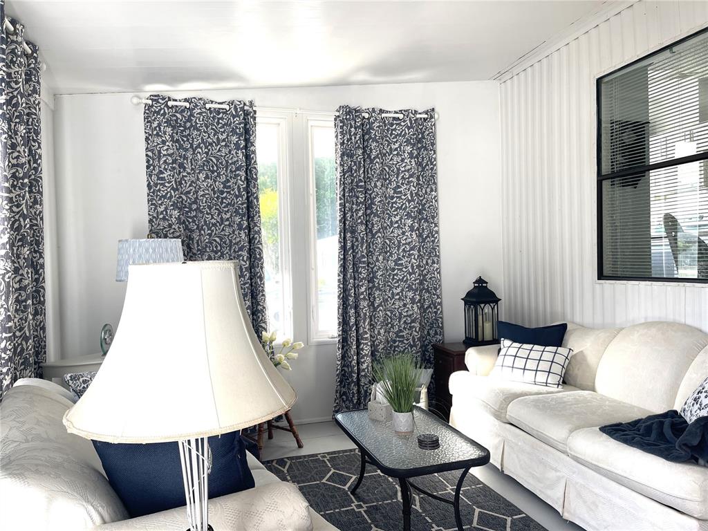 A living room features white walls, patterned blue curtains, a white sofa, and a glass-topped table — 312 S TIMBER TRL, WILDWOOD, FL
