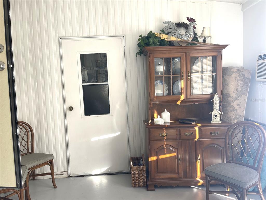 A sunroom features a white door, a wooden hutch, and two wicker chairs — 312 S TIMBER TRL, WILDWOOD, FL