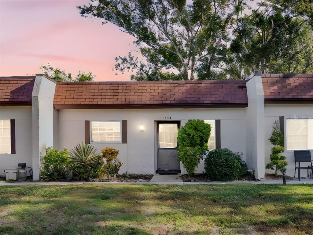 A single-story townhouse exterior with a brown shingled roof, white stucco walls, and front landscaping — 3109 MISSION GROVE DRIVE UNIT D, PALM HARBOR, FL