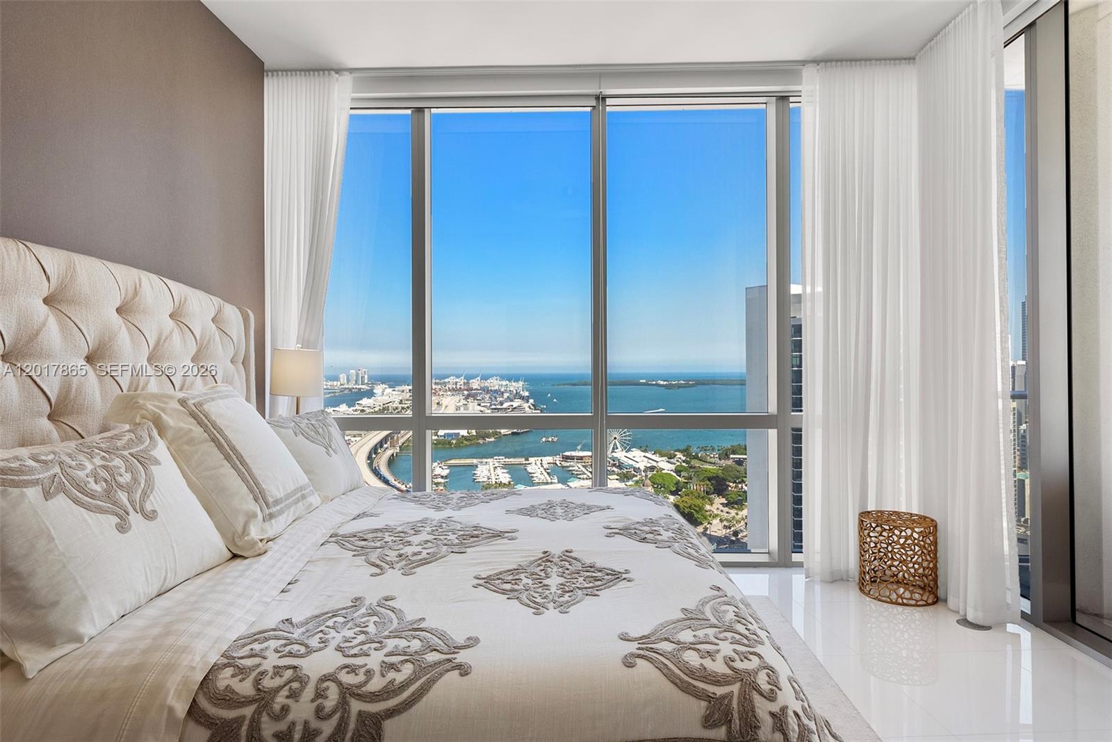 A bedroom features a tufted headboard, white bedding, and floor-to-ceiling windows overlooking a harbor — 851 NE 1st Ave # 3711, Miami FL 33132, MIAMI, FL