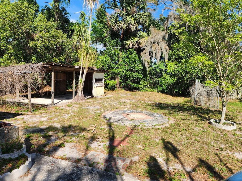A backyard features a small open-sided shed, a circular stone patio, and mature trees — 2319 S SUMMERLIN AVENUE, SANFORD, FL