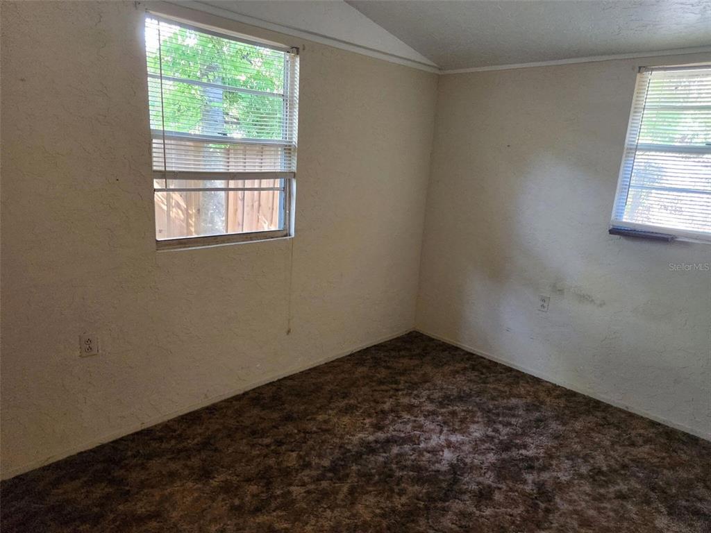 An empty room features beige walls, brown patterned carpeting, and two windows with blinds — 2319 S SUMMERLIN AVENUE, SANFORD, FL
