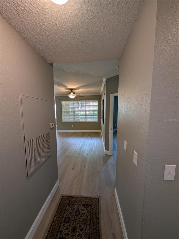 A hallway with light wood-look flooring leads into a living area with a ceiling fan — 2632 ROBERT TRENT JONES DRIVE UNIT 110, ORLANDO, FL