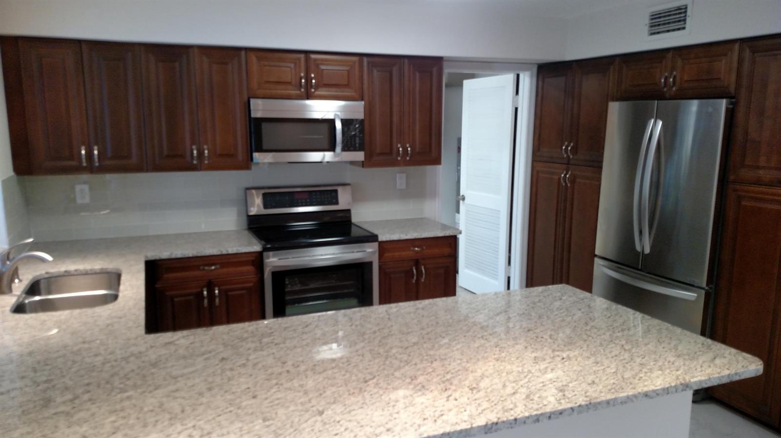 A kitchen features dark wood cabinets, stainless steel appliances, and light granite countertops — 451 W Conference Drive, Boca Raton FL 33486, BOCA RATON, FL