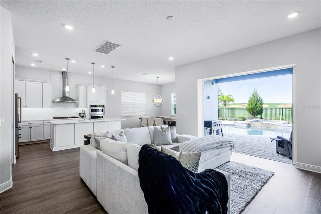 An open-concept living room and kitchen overlook a patio with a pool and golf course — 15734 VETTA DRIVE, MONTVERDE, FL