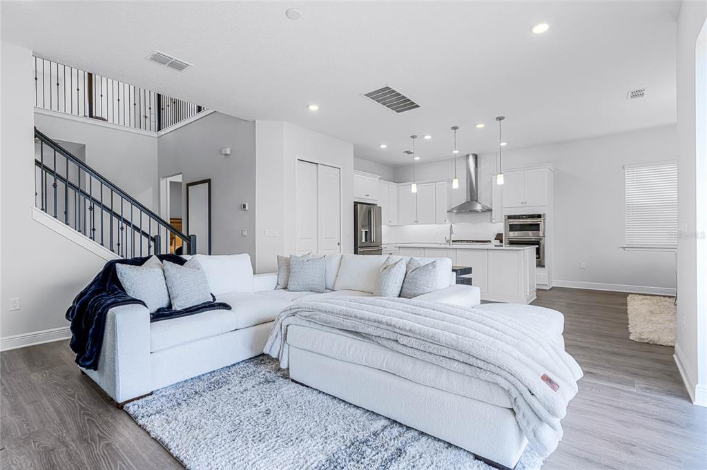 A bright living room features a white sectional sofa, a staircase, and an open kitchen — 15734 VETTA DRIVE, MONTVERDE, FL