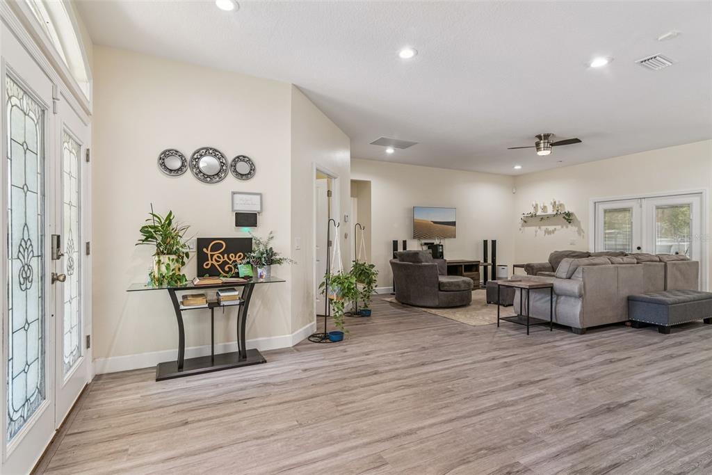 A bright living room features light wood-look flooring, a glass console table, and gray furniture — 5211 SW 103RD LOOP, OCALA, FL