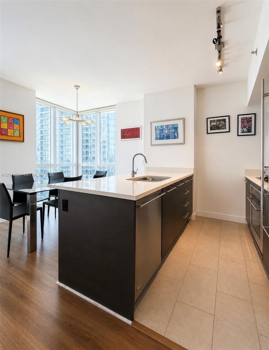 A modern kitchen features a dark island with a sink, white countertops, and dining area — 55 SE 6th St # 2802, Miami FL 33131, MIAMI, FL