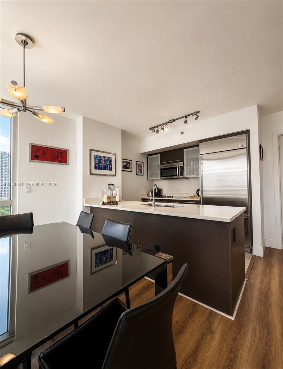 A modern kitchen with dark cabinetry and stainless steel appliances overlooks a glass dining table — 55 SE 6th St # 2802, Miami FL 33131, MIAMI, FL
