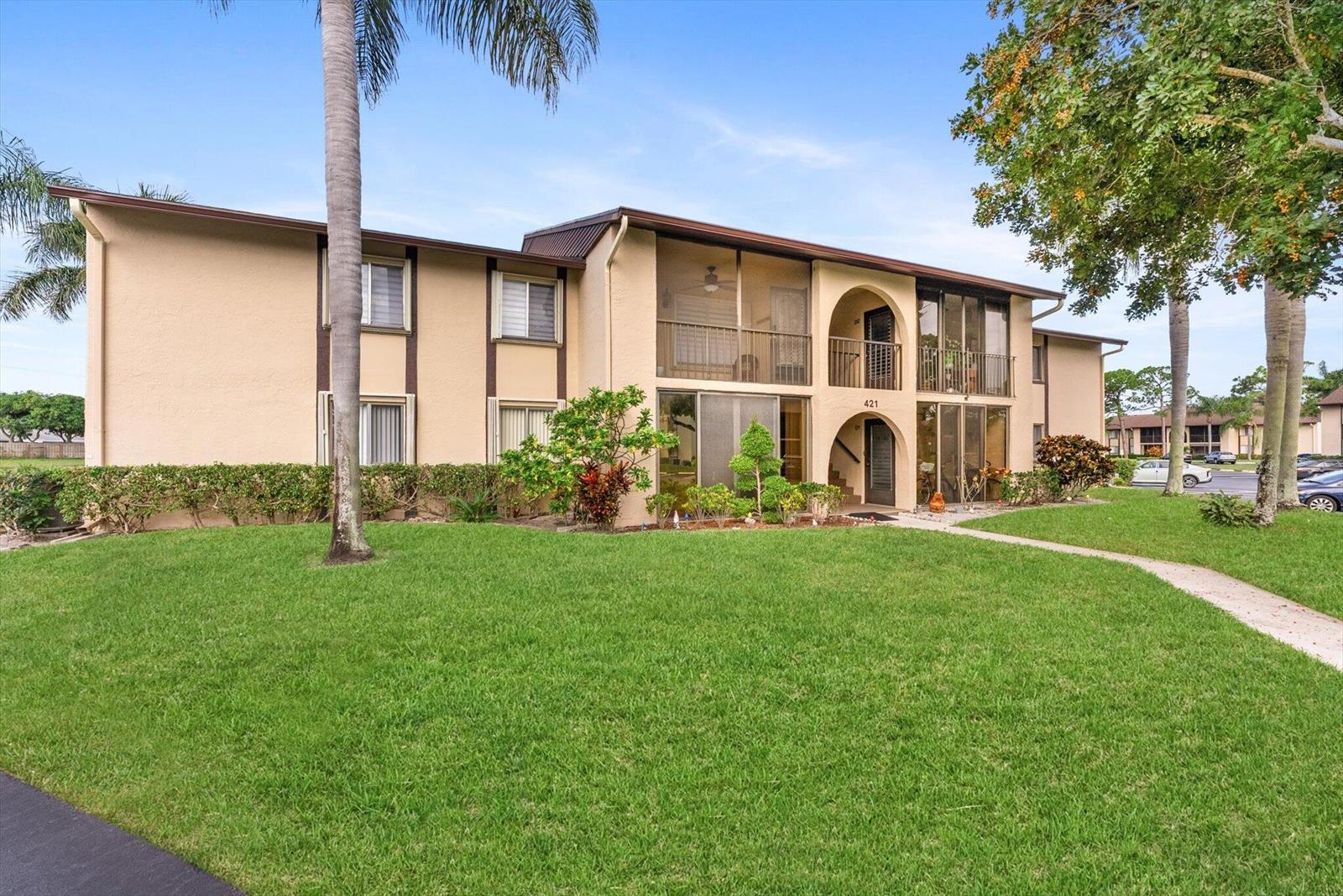 A two-story apartment building with tan stucco walls and screened balconies sits on a lawn — 421 Pine Glen Lane # A2, FL 33463, FL