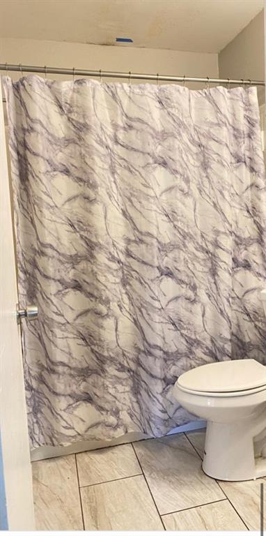 A bathroom features a marble-patterned shower curtain, a white toilet, and light-colored tile flooring — 2412 MARSHALL AVENUE, SANFORD, FL