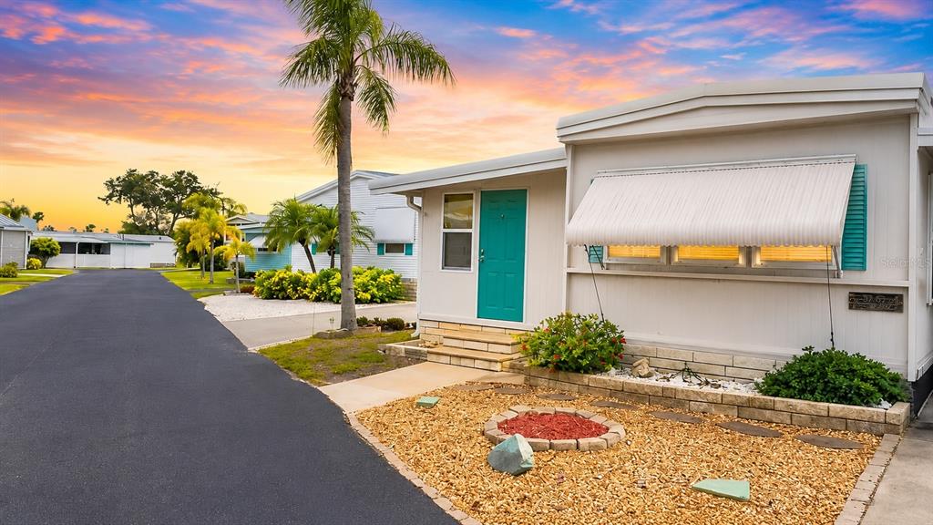 A single-story mobile home features a teal front door, white siding, and a gravel yard — 7234 MOUNT FAIRFIELD ROAD NE UNIT 529, ST PETERSBURG, FL