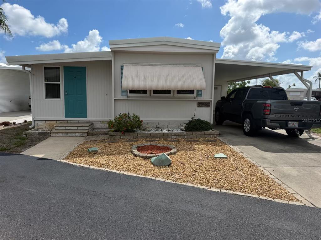 A single-story manufactured home with a teal front door, metal awning, and attached carport — 7234 MOUNT FAIRFIELD ROAD NE UNIT 529, ST PETERSBURG, FL