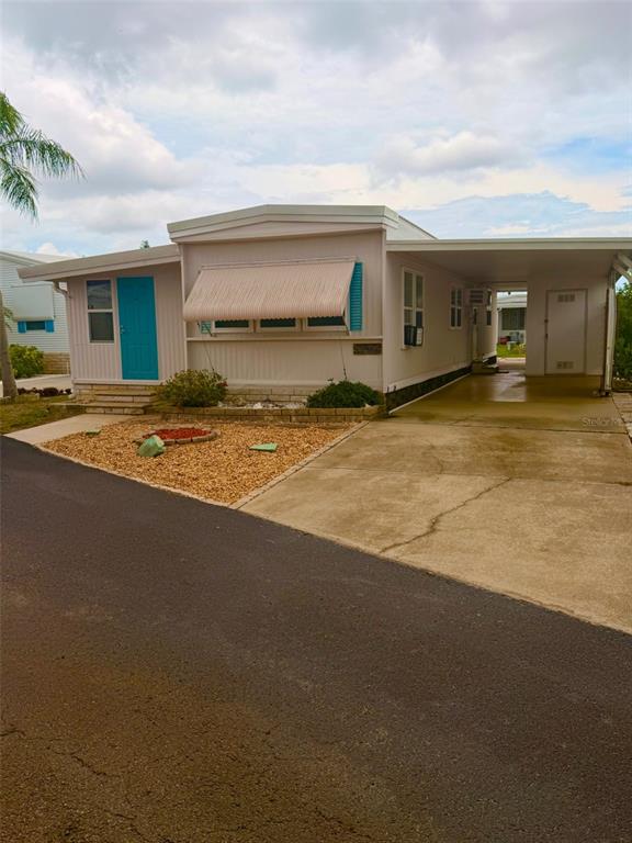 A mobile home exterior features a teal front door, concrete steps, and a gravel yard — 7234 MOUNT FAIRFIELD ROAD NE UNIT 529, ST PETERSBURG, FL