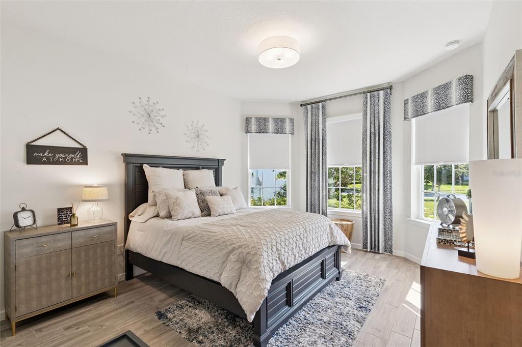 A bedroom features a dark wood bed frame, light wood-look flooring, and three windows with curtains — 13940 DESTIN BEACH LANE, ORLANDO, FL
