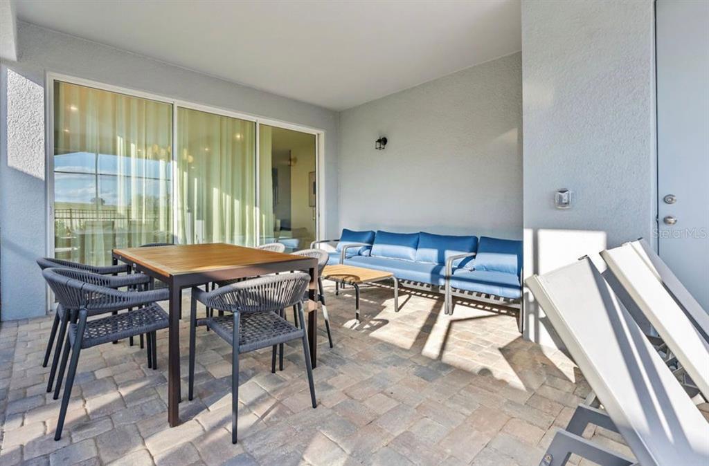 A covered patio features a dining set, a blue sofa, and light-colored stone pavers — 9144 DRIFTWOOD PATH, KISSIMMEE, FL