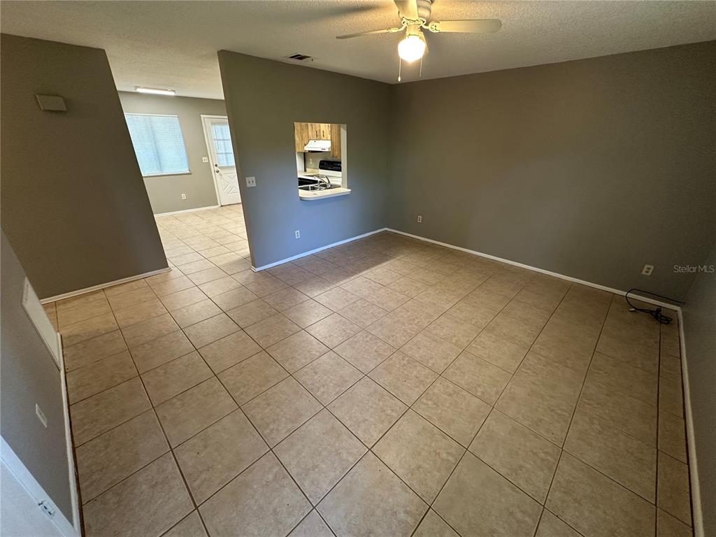 An open-concept living area features beige tile flooring, gray walls, and a kitchen pass-through window — 1916 WIZARD COURT, LONGWOOD, FL
