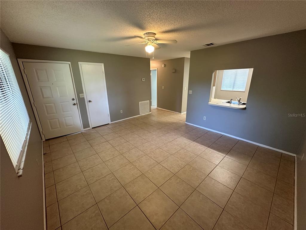 An empty room features beige tile flooring, gray walls, a ceiling fan, and a pass-through window — 1916 WIZARD COURT, LONGWOOD, FL