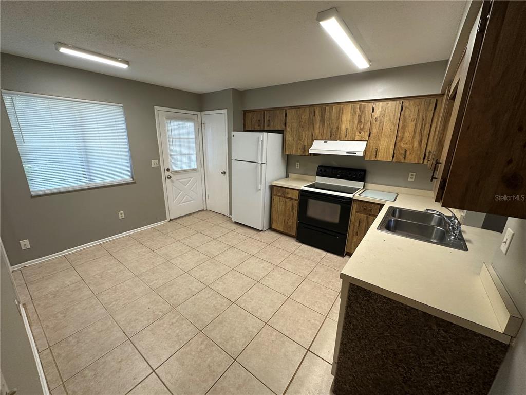 A kitchen with wood cabinets, white appliances, tile flooring, and a window with blinds — 1916 WIZARD COURT, LONGWOOD, FL