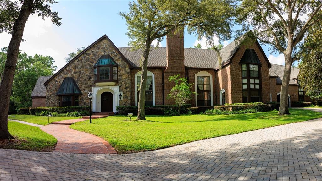 A large brick and stone house with a circular driveway and mature trees at dusk — 810 SWEETWATER CLUB BOULEVARD, LONGWOOD, FL