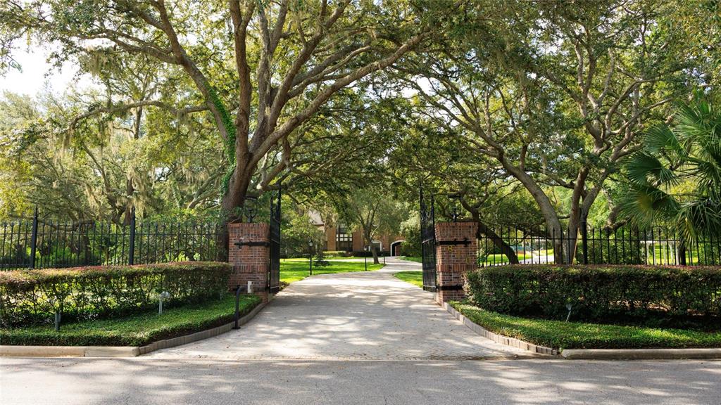 A large brick house with a paved driveway and mature trees at dusk — 810 SWEETWATER CLUB BOULEVARD, LONGWOOD, FL