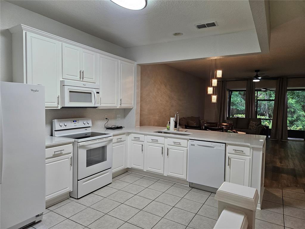 A kitchen with white cabinets, white appliances, and a peninsula overlooking a living area — 5166 HAWKSTONE DRIVE, SANFORD, FL