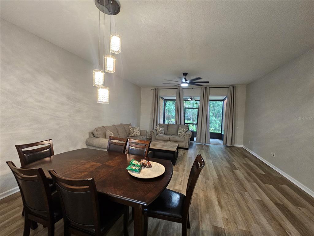 A dining area with a pendant light fixture opens into a living room with wood-look flooring — 5166 HAWKSTONE DRIVE, SANFORD, FL