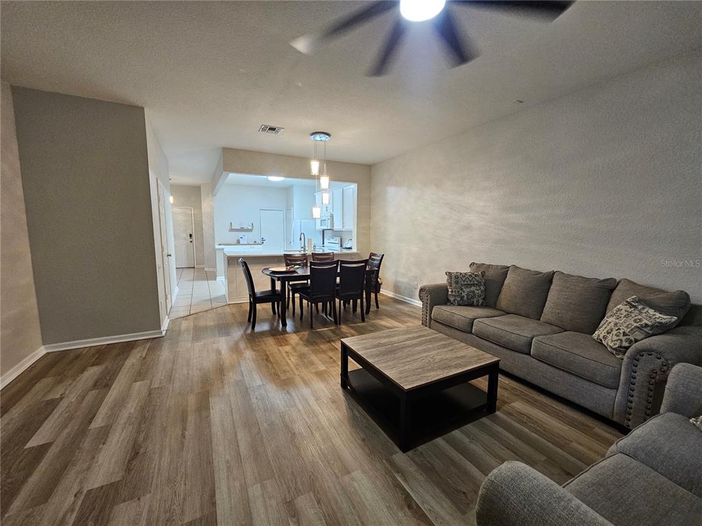 An open-concept living and dining area features wood-look flooring, a gray sofa, and kitchen access — 5166 HAWKSTONE DRIVE, SANFORD, FL