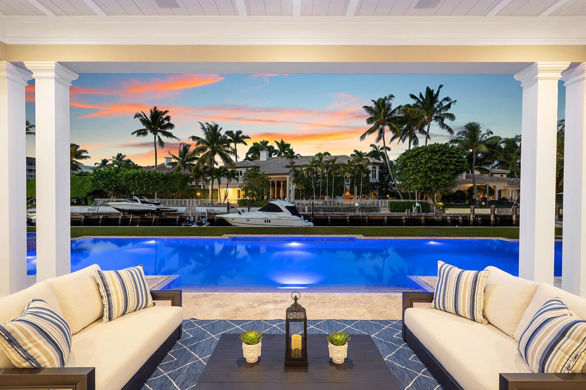 A covered patio with two sofas overlooks a swimming pool, a canal, and palm trees — 133 W Coconut Palm Road, Boca Raton FL 33432, BOCA RATON, FL