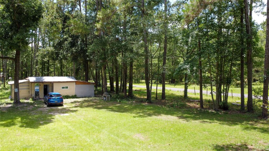 A small, light-colored house with a blue car parked in front sits near a wooded area — 18864 N HIGHWAY 329, MICANOPY, FL