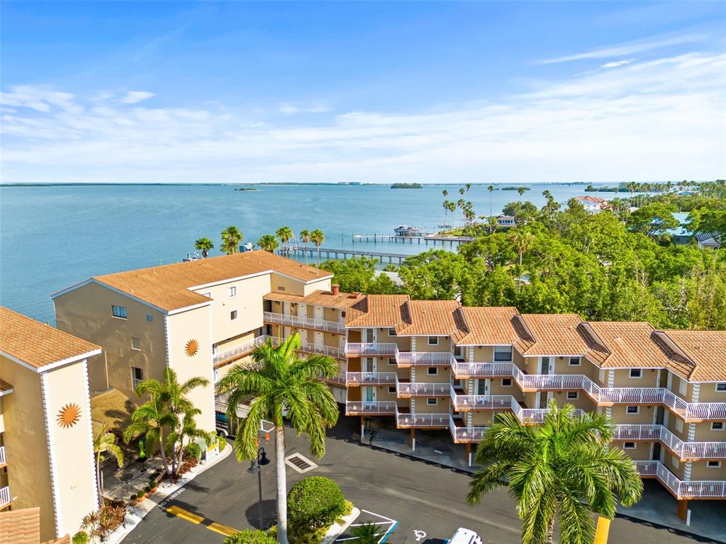 An aerial view shows a multi-story apartment building with a tiled roof near the water — 1420 BAYSHORE BOULEVARD UNIT 206, DUNEDIN, FL