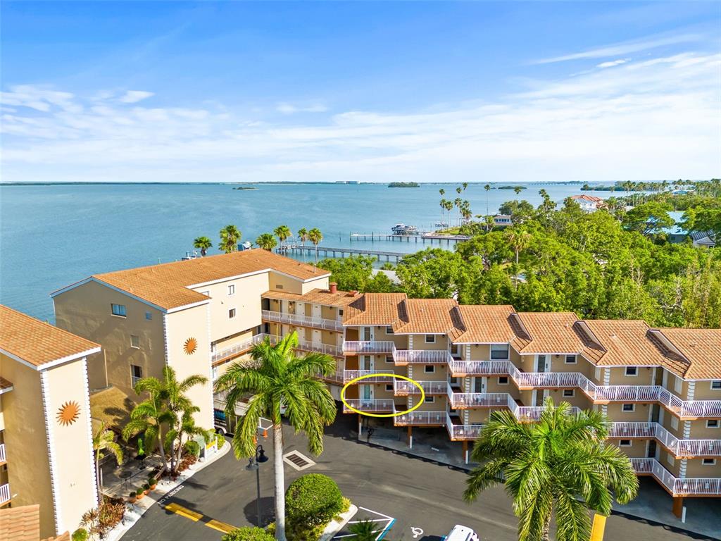 An aerial view shows a multi-story apartment building with a yellow-circled balcony overlooking water — 1420 BAYSHORE BOULEVARD UNIT 206, DUNEDIN, FL