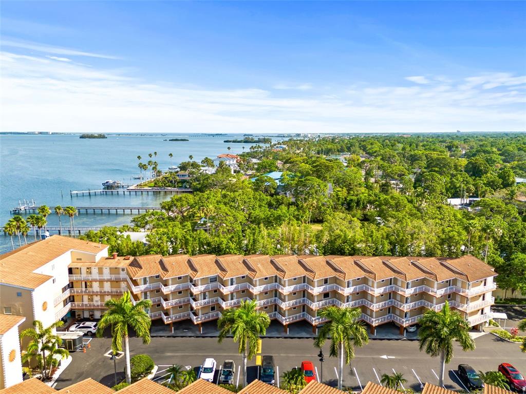 An aerial view shows a multi-story apartment building with a parking lot and waterfront docks — 1420 BAYSHORE BOULEVARD UNIT 206, DUNEDIN, FL
