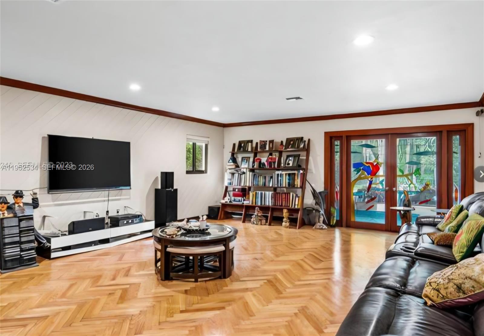 A living room features herringbone wood floors, a wall-mounted television, a bookshelf, and glass doors — 3420 SW 129th Ave, Miami FL 33175, MIAMI, FL