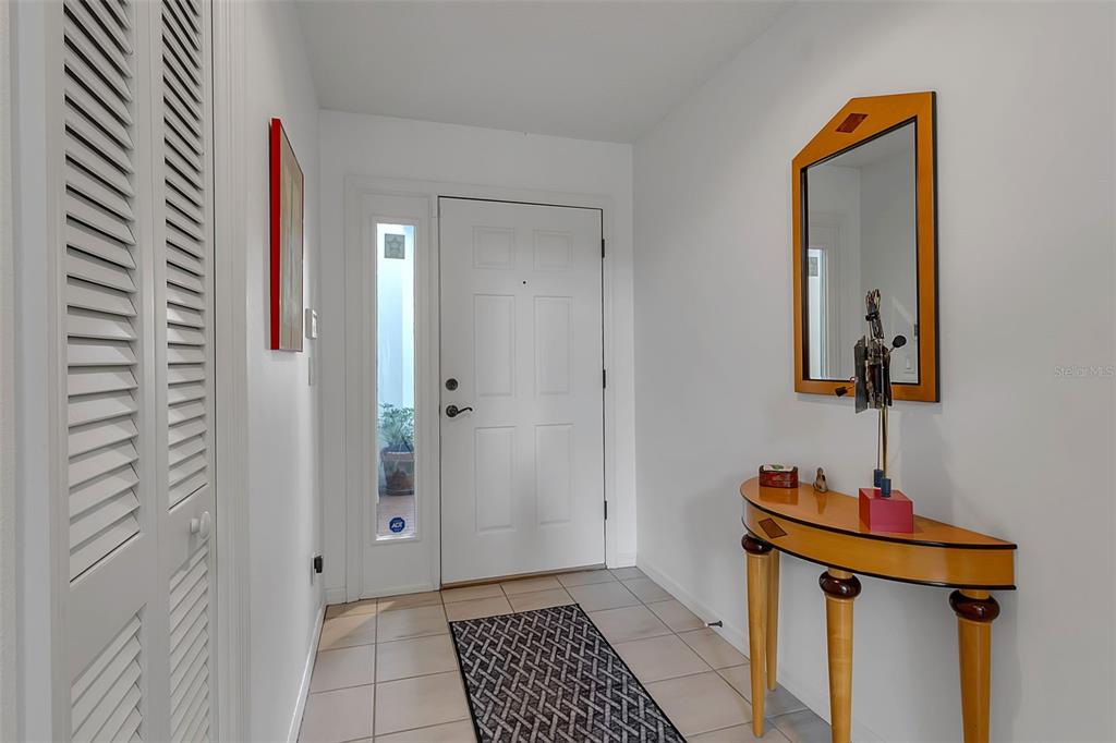 A bright entryway features a white front door, tiled floor, console table, and wall mirror — 4360 CAMINO MADERA, SARASOTA, FL