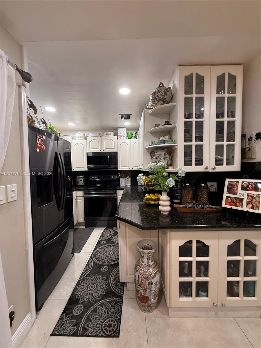 A kitchen features white cabinetry, black countertops, a black refrigerator, and a patterned floor runner — 4100 Crystal Lake Dr # 111, Deerfield Beach FL 33064, DEERFIELD BEACH, FL