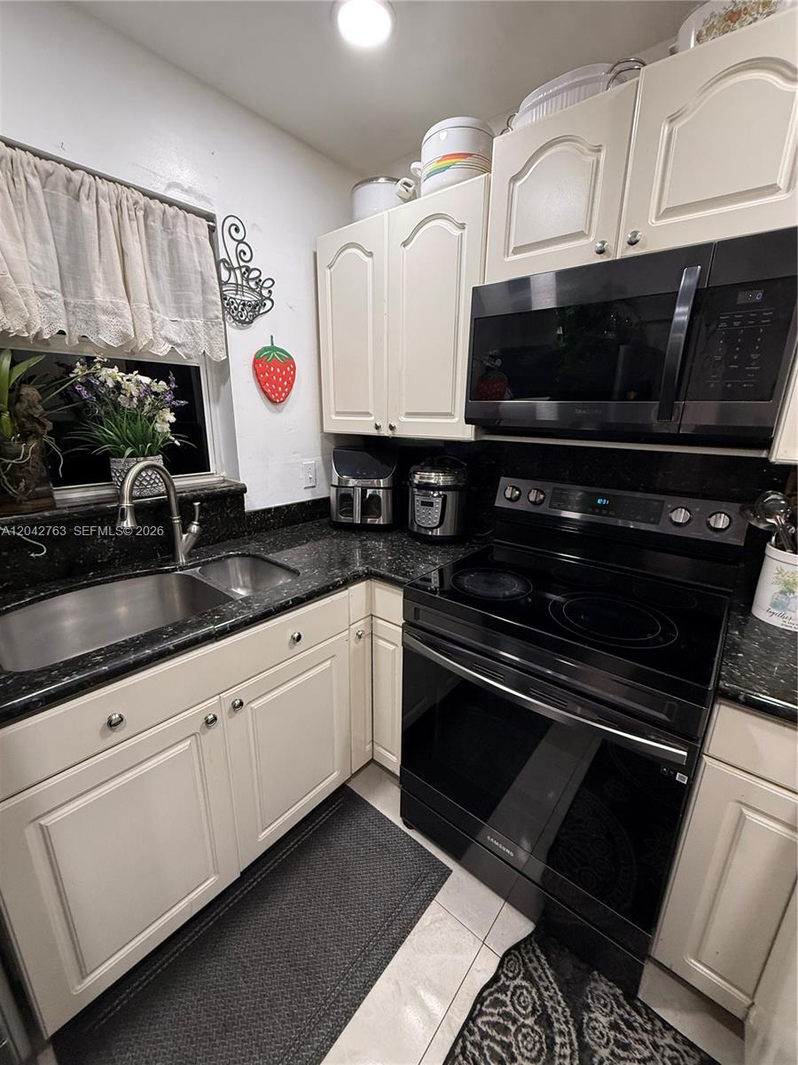 A kitchen features white cabinets, black countertops, a stainless steel sink, and black appliances — 4100 Crystal Lake Dr # 111, Deerfield Beach FL 33064, DEERFIELD BEACH, FL
