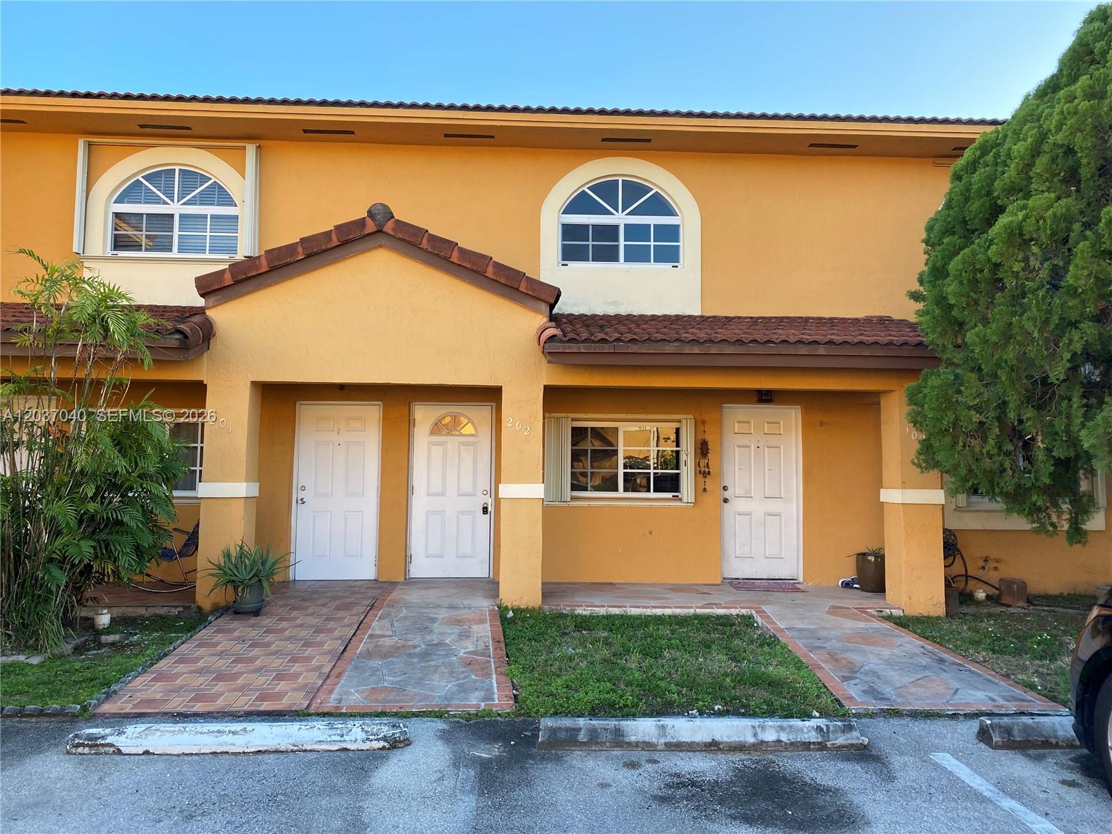 A two-story yellow stucco townhouse exterior features arched windows, tiled roofs, and three white doors — 3566 W 80th St # 57, Hialeah FL 33018, HIALEAH, FL