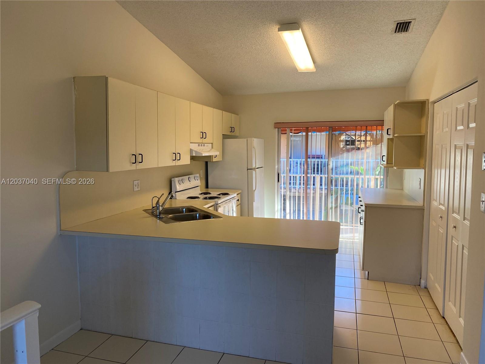 A kitchen features white cabinets, a tiled breakfast bar, and a sliding glass door — 3566 W 80th St # 57, Hialeah FL 33018, HIALEAH, FL