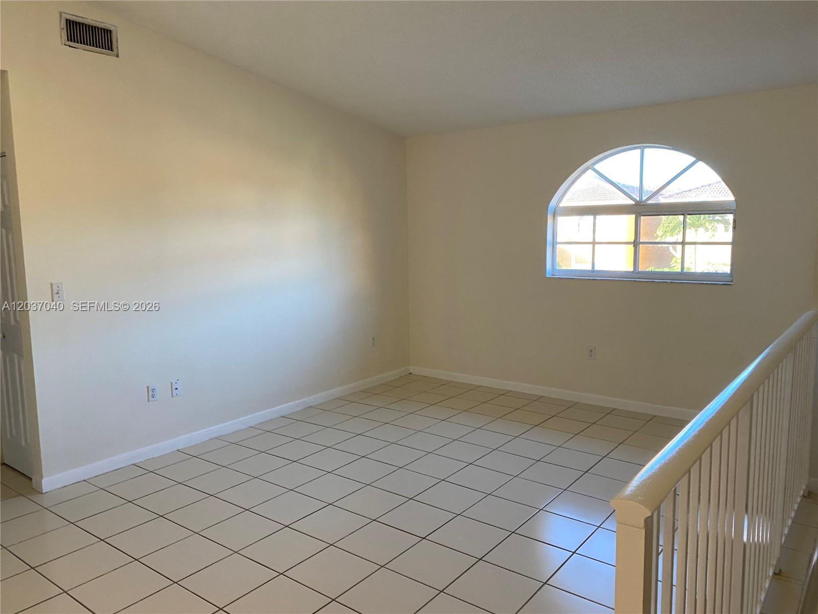 An empty room features white tile flooring, beige walls, and an arched window — 3566 W 80th St # 57, Hialeah FL 33018, HIALEAH, FL