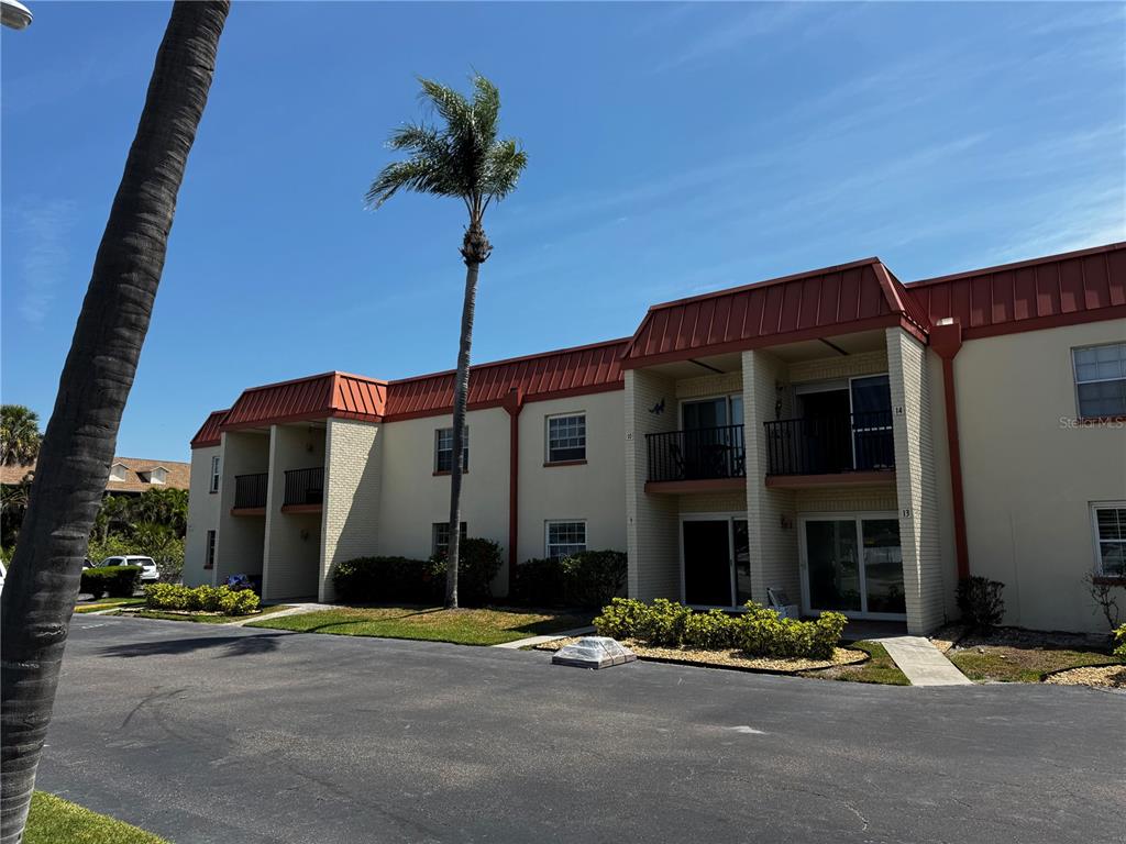 A two-story brick apartment building features a red metal roof and an exterior staircase — 10365 PARADISE BOULEVARD UNIT 9, TREASURE ISLAND, FL