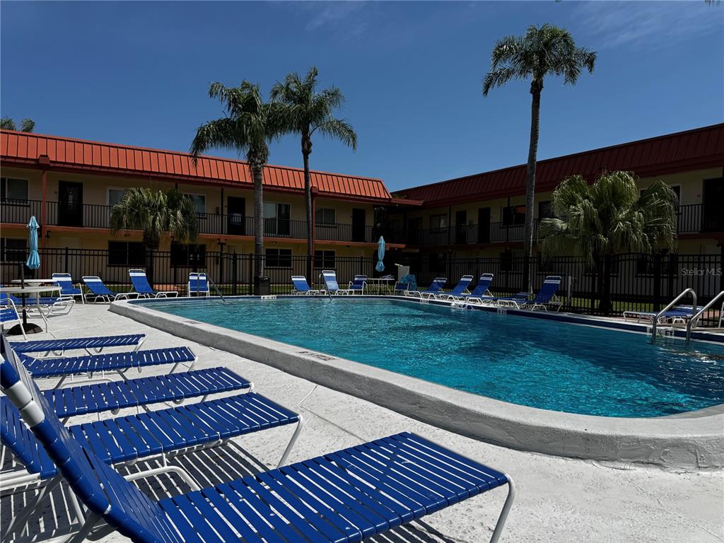 A swimming pool surrounded by blue lounge chairs and palm trees in front of apartments — 10365 PARADISE BOULEVARD UNIT 9, TREASURE ISLAND, FL