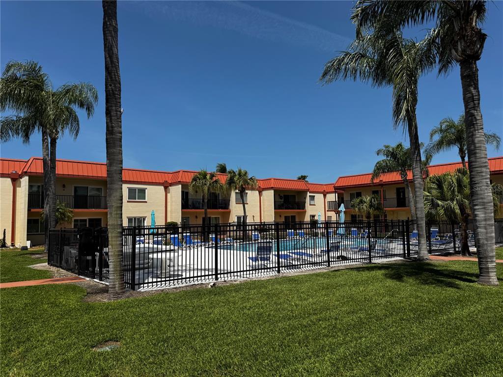 An outdoor swimming pool is surrounded by a black metal fence and apartment buildings — 10365 PARADISE BOULEVARD UNIT 9, TREASURE ISLAND, FL